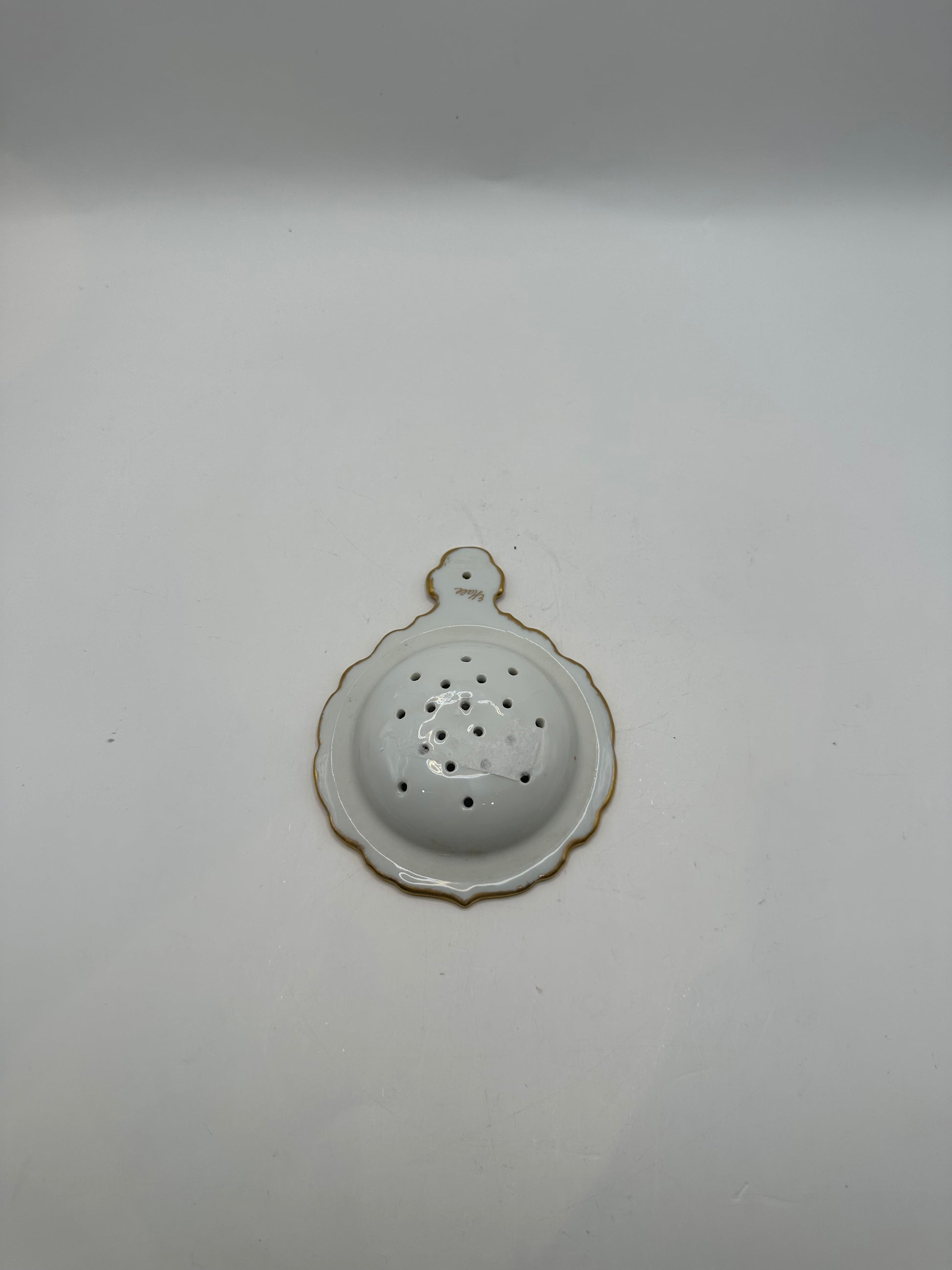 Reverse of the gold-trimmed porcelain tea strainer showing the scalloped white underside