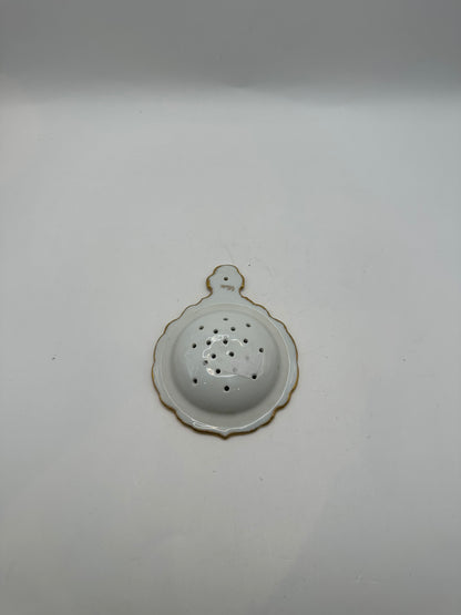 Reverse of the gold-trimmed porcelain tea strainer showing the scalloped white underside