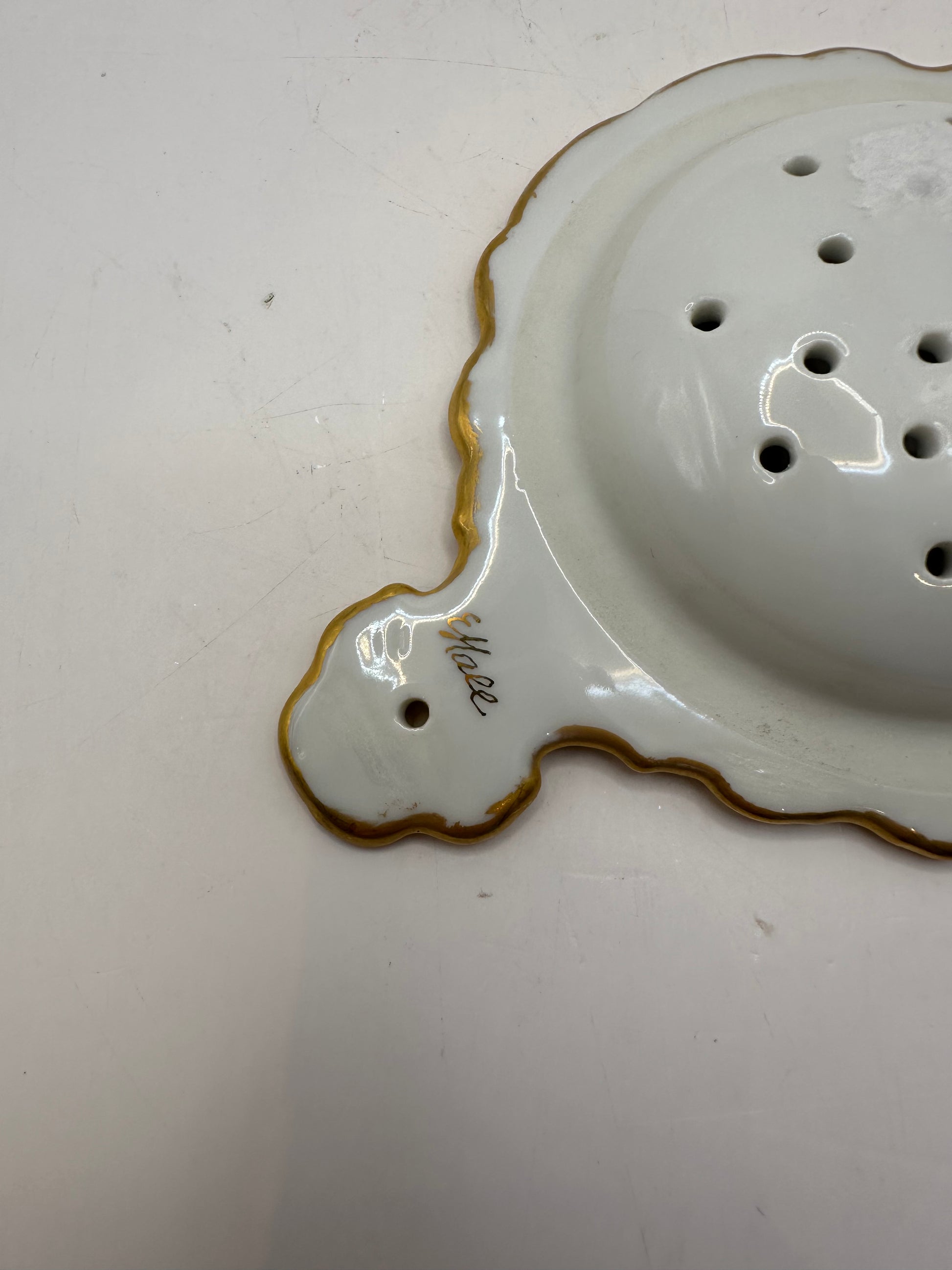 Close-up of the tea strainer's gold-trimmed handle with a hand-painted script signature
