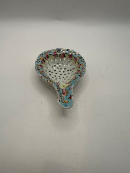 Angled view of the hand-painted porcelain tea strainer with pink floral and gold accents
