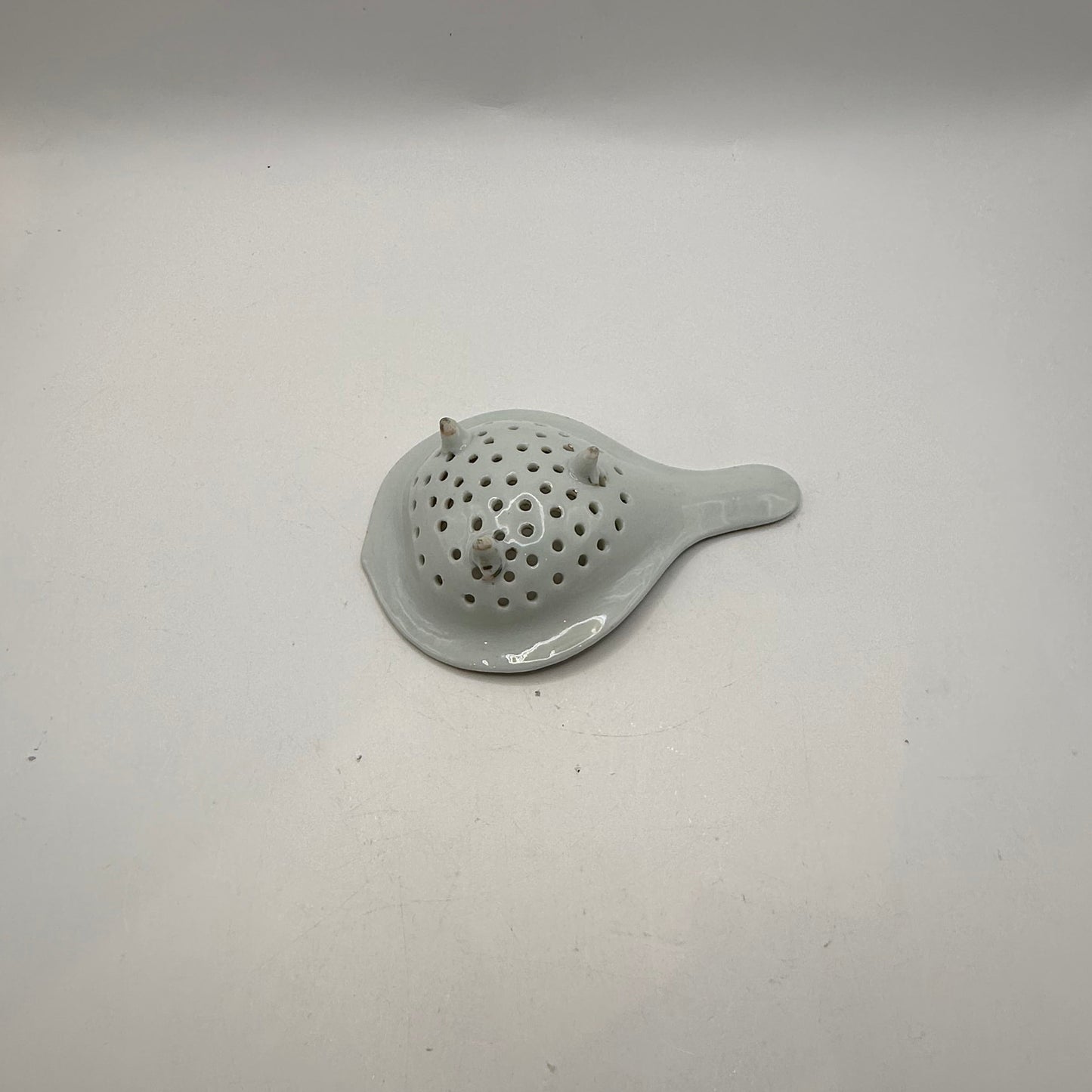 Underside of the porcelain tea strainer showing its three small feet and white glaze