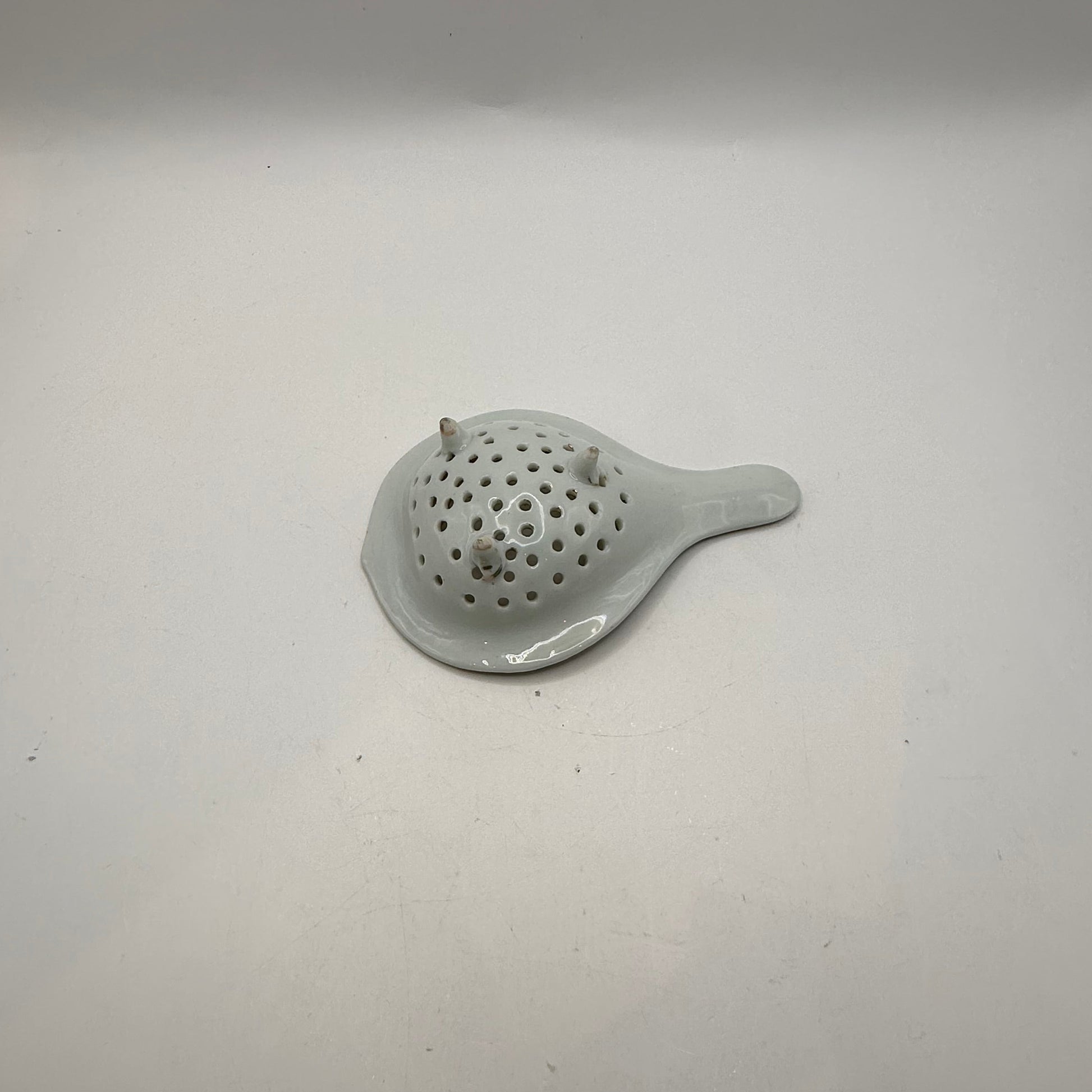 Underside of the porcelain tea strainer showing its three small feet and white glaze