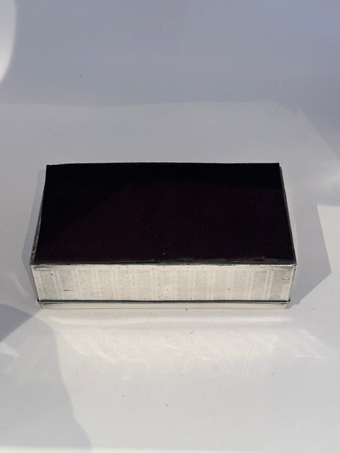 Closed cigarette box viewed at an angle, lid in shadow over ribbed silver-plate sides