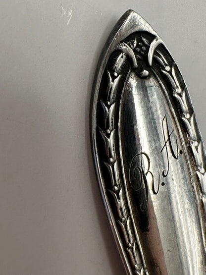 Close-up of a spoon handle with laurel design and engraved 'R.A.' monogram