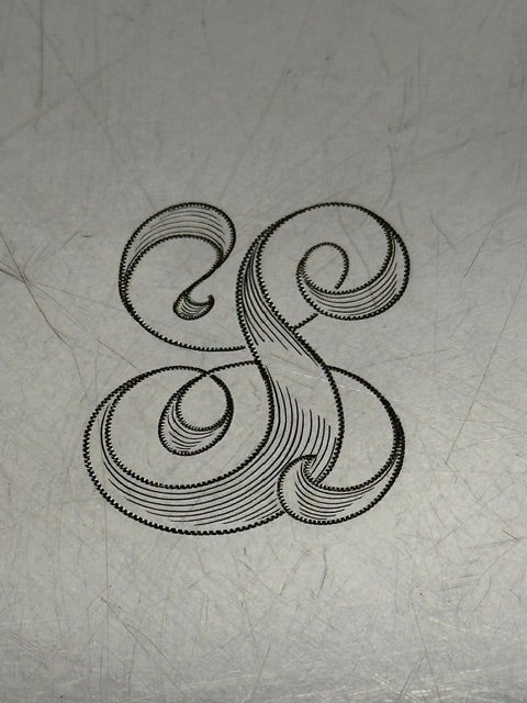 Close-up of the ornate engraved script monogram at the center of the tray