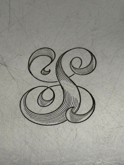 Close-up of the ornate engraved script monogram at the center of the tray