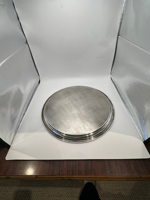 Round silver-plate tray photographed in a light box, raised angled view
