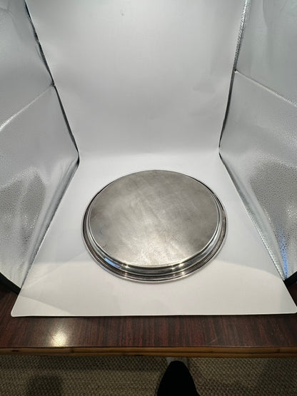 Round silver-plate tray photographed in a light box, raised angled view