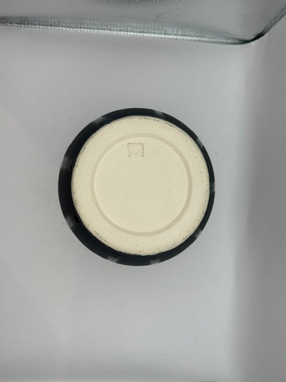 Underside of the black ceramic vessel showing cream foot ring and incised maker's mark