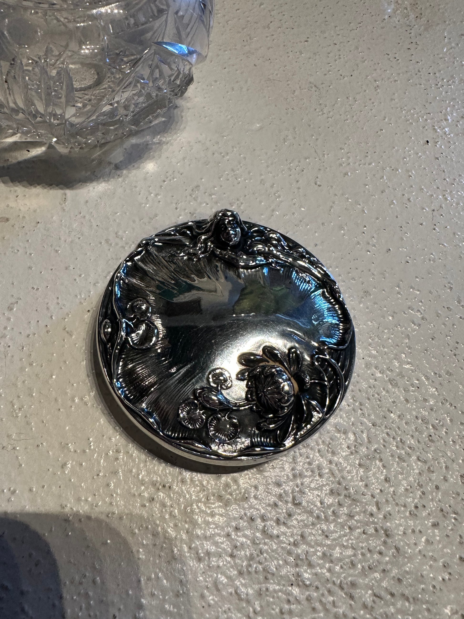 Sterling silver dresser jar lid with Art Nouveau floral motifs beside cut-crystal base