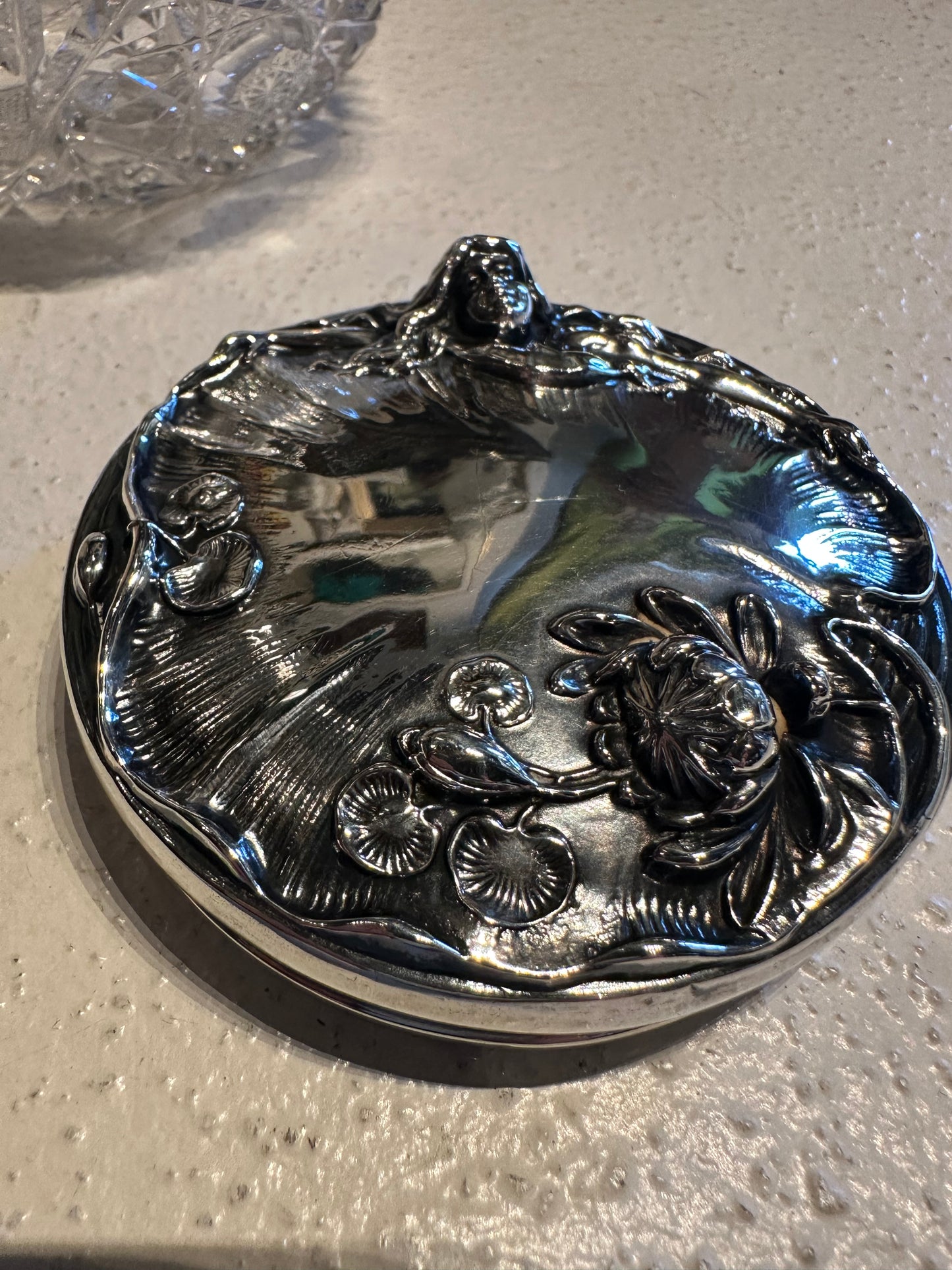Detached ornate sterling silver dresser jar lid with floral repousse, top view on counter