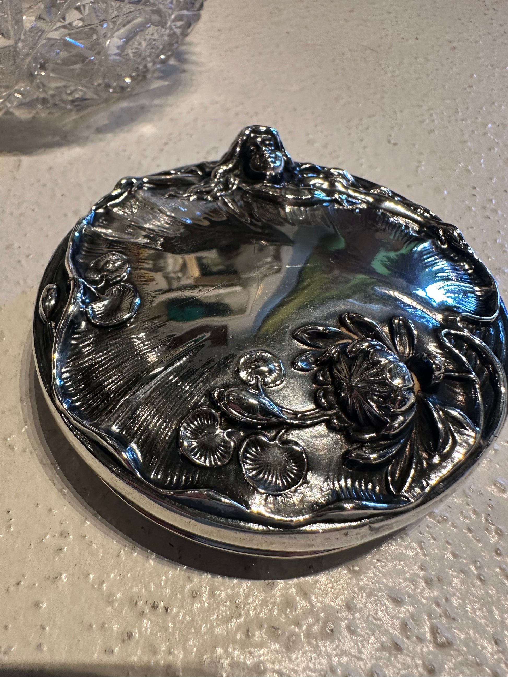 Detached ornate sterling silver dresser jar lid with floral repousse, top view on counter