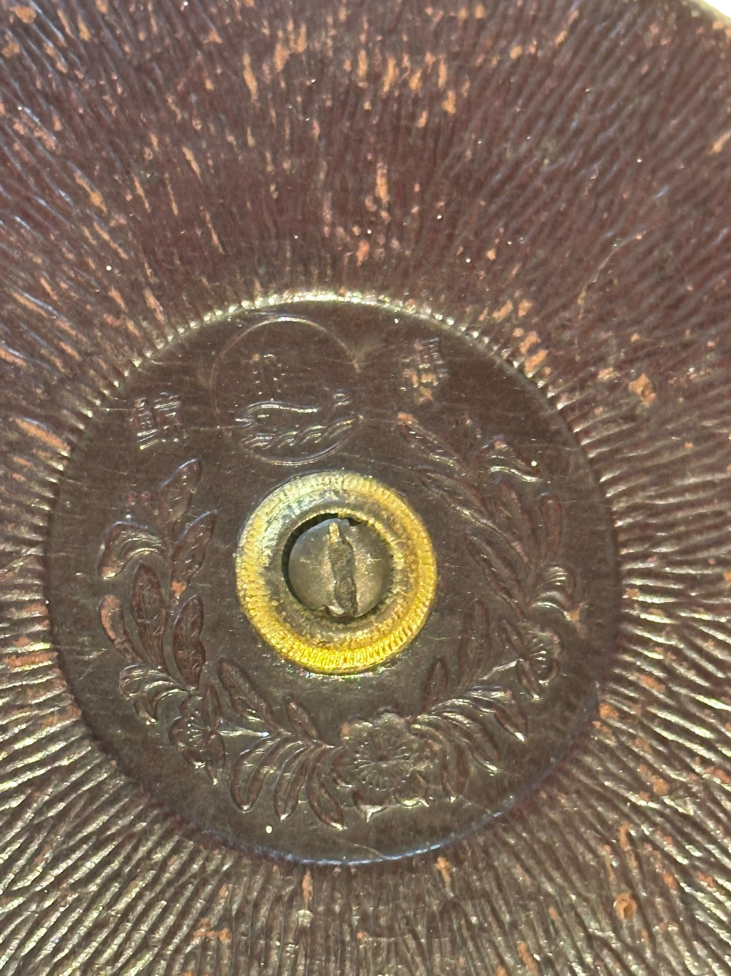Close-up of the antique tape measure's embossed floral center and brass winding fitting