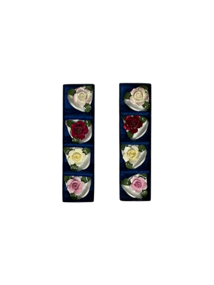 Set of eight porcelain rose place card holders in pink, red and cream, shown in two navy boxes