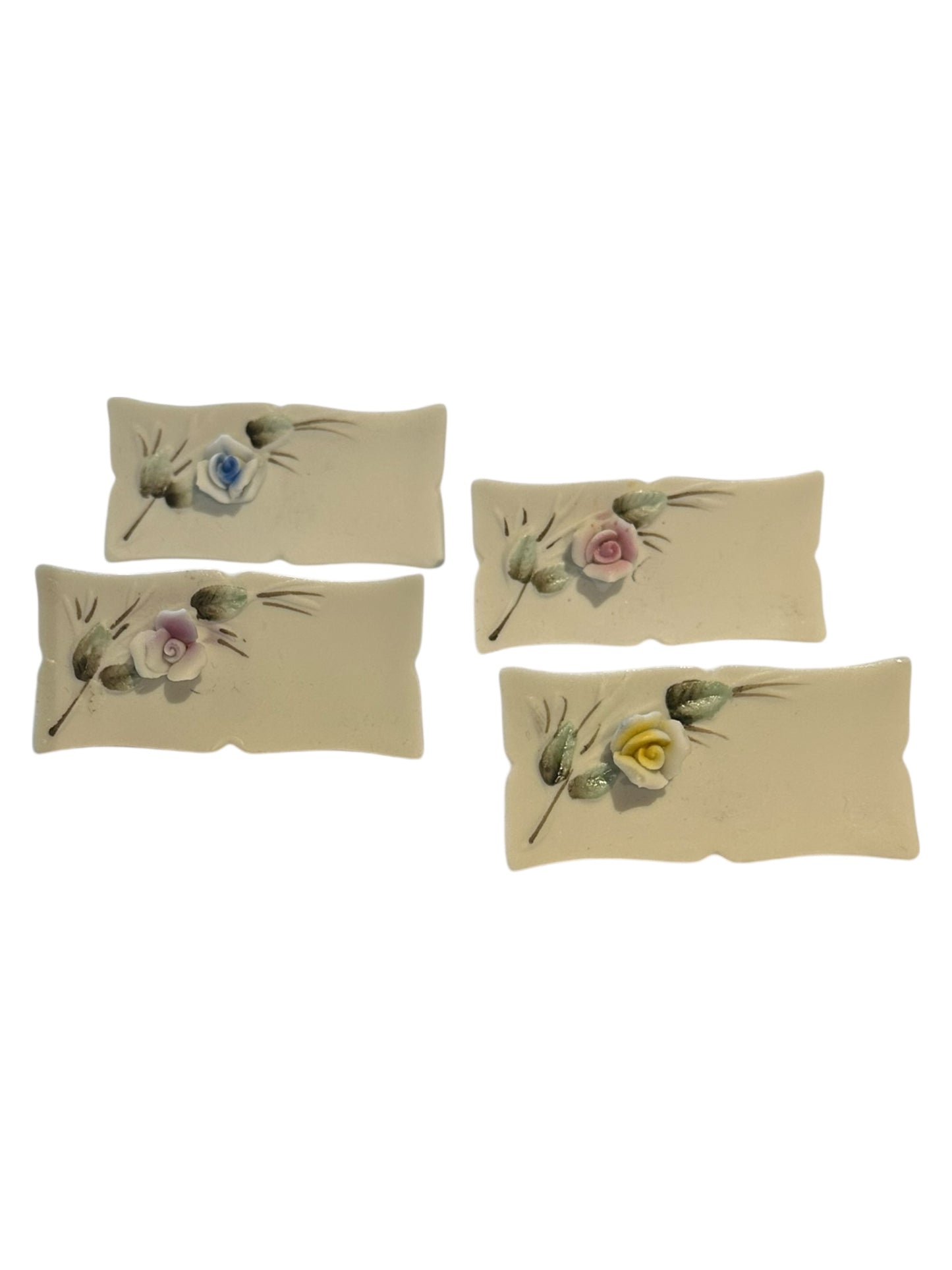 Four white porcelain floral place card holders arranged diagonally, each with a pastel flower spray