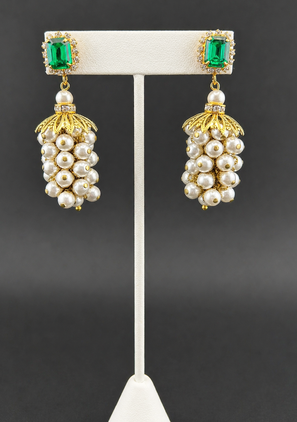 Pearl cluster drop earrings with emerald-green crystal tops, displayed on a white earring stand