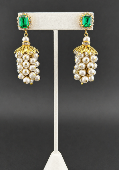 Pearl cluster drop earrings with emerald-green crystal tops, displayed on a white earring stand