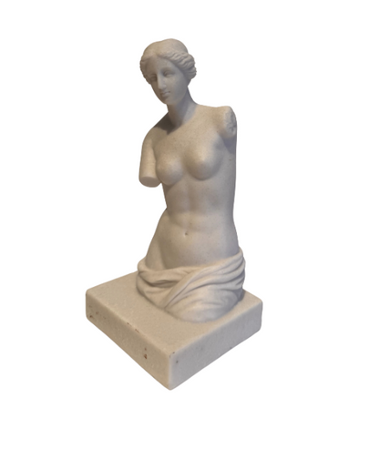 Off-white classical Venus de Milo sculpture depicting a female figure with wavy hair arranged in a bun, a softly detailed face, an armless torso, and draped fabric around the hips. The sculpture stands on a rectangular base with subtle speckling and minor surface discoloration.