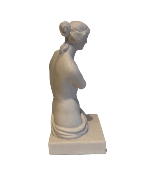 Off-white classical Venus de Milo sculpture depicting a female figure with wavy hair arranged in a bun, a softly detailed face, an armless torso, and draped fabric around the hips. The sculpture stands on a rectangular base with subtle speckling and minor surface discoloration.