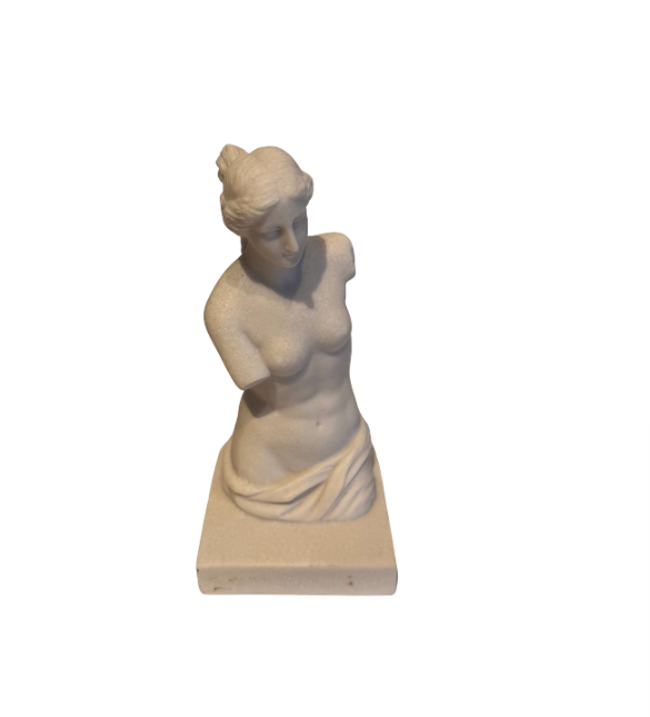 Off-white classical Venus de Milo sculpture depicting a female figure with wavy hair arranged in a bun, a softly detailed face, an armless torso, and draped fabric around the hips. The sculpture stands on a rectangular base with subtle speckling and minor surface discoloration.