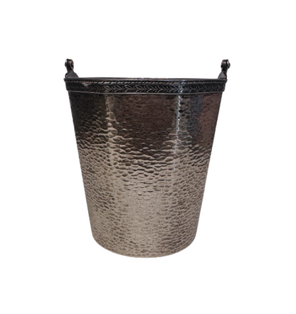 A vintage silver-tone metal ice bucket with a hexagonal, slightly tapered body and a textured hammered surface. A narrow decorative band with a repeating leaf pattern encircles the upper rim. A flat metal carrying handle is attached to opposite sides of the bucket and can be raised or lowered. The matching metal ice tongs feature textured arms ending in three-pronged bird claw shapes. The bucket's interior has a hammered texture with visible darkening and discoloration at the bottom.