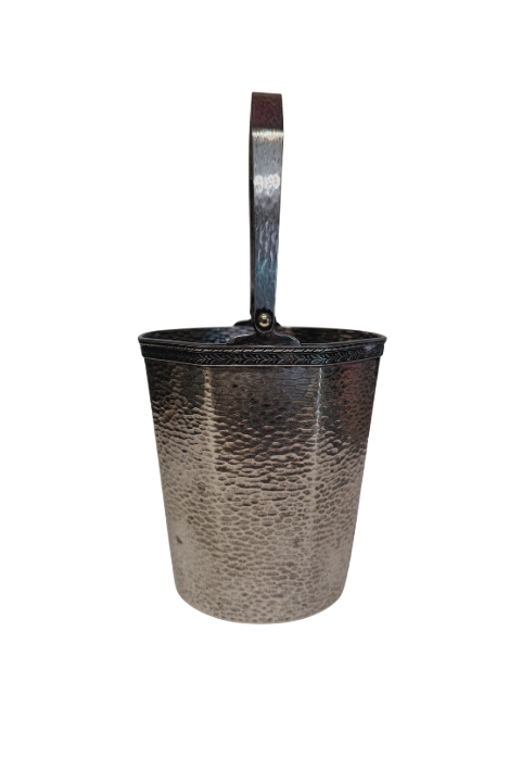 A vintage silver-tone metal ice bucket with a hexagonal, slightly tapered body and a textured hammered surface. A narrow decorative band with a repeating leaf pattern encircles the upper rim. A flat metal carrying handle is attached to opposite sides of the bucket and can be raised or lowered. The matching metal ice tongs feature textured arms ending in three-pronged bird claw shapes. The bucket's interior has a hammered texture with visible darkening and discoloration at the bottom.