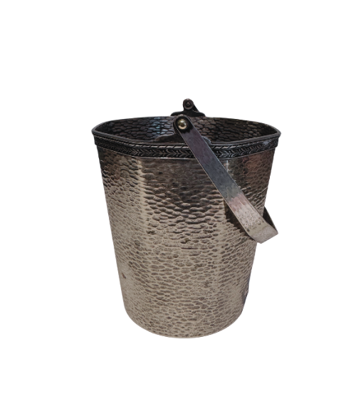 A vintage silver-tone metal ice bucket with a hexagonal, slightly tapered body and a textured hammered surface. A narrow decorative band with a repeating leaf pattern encircles the upper rim. A flat metal carrying handle is attached to opposite sides of the bucket and can be raised or lowered. The matching metal ice tongs feature textured arms ending in three-pronged bird claw shapes. The bucket's interior has a hammered texture with visible darkening and discoloration at the bottom.