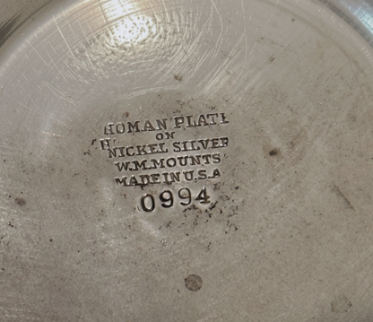 A vintage silver-tone metal ice bucket with a hexagonal, slightly tapered body and a textured hammered surface. A narrow decorative band with a repeating leaf pattern encircles the upper rim. A flat metal carrying handle is attached to opposite sides of the bucket and can be raised or lowered. The matching metal ice tongs feature textured arms ending in three-pronged bird claw shapes. The bucket's interior has a hammered texture with visible darkening and discoloration at the bottom.
