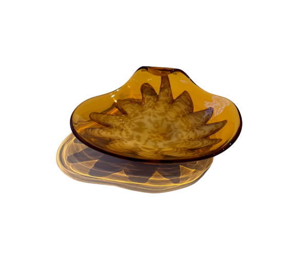 Vintage translucent amber glass dish with an irregular curved rim and a raised cream-and-brown swirled floral starburst design in the center.