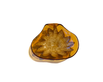 Vintage translucent amber glass dish with an irregular curved rim and a raised cream-and-brown swirled floral starburst design in the center.