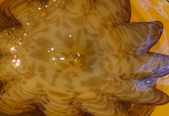 Vintage translucent amber glass dish with an irregular curved rim and a raised cream-and-brown swirled floral starburst design in the center.