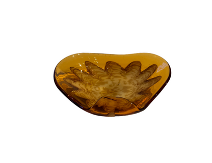Vintage translucent amber glass dish with an irregular curved rim and a raised cream-and-brown swirled floral starburst design in the center.