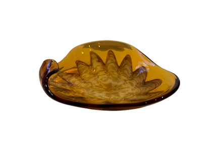 Vintage translucent amber glass dish with an irregular curved rim and a raised cream-and-brown swirled floral starburst design in the center.