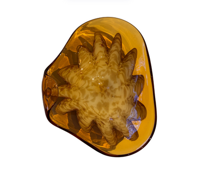 Vintage translucent amber glass dish with an irregular curved rim and a raised cream-and-brown swirled floral starburst design in the center.