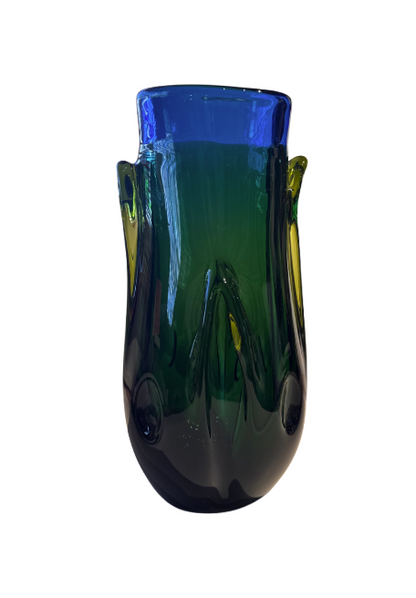 Tall, sculptural glass vase with a deep emerald green body, rounded base, and thick cobalt blue rim. Raised, flowing glass accents extend along the sides, incorporating translucent yellow-green details. The vase has an irregular oval opening and a glossy, reflective surface.