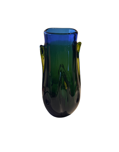 Tall, sculptural glass vase with a deep emerald green body, rounded base, and thick cobalt blue rim. Raised, flowing glass accents extend along the sides, incorporating translucent yellow-green details. The vase has an irregular oval opening and a glossy, reflective surface.