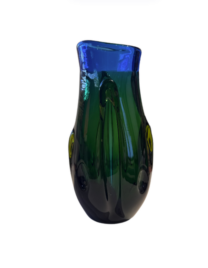 Tall, sculptural glass vase with a deep emerald green body, rounded base, and thick cobalt blue rim. Raised, flowing glass accents extend along the sides, incorporating translucent yellow-green details. The vase has an irregular oval opening and a glossy, reflective surface.