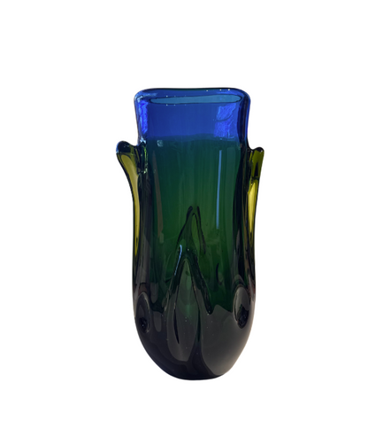 Tall, sculptural glass vase with a deep emerald green body, rounded base, and thick cobalt blue rim. Raised, flowing glass accents extend along the sides, incorporating translucent yellow-green details. The vase has an irregular oval opening and a glossy, reflective surface.