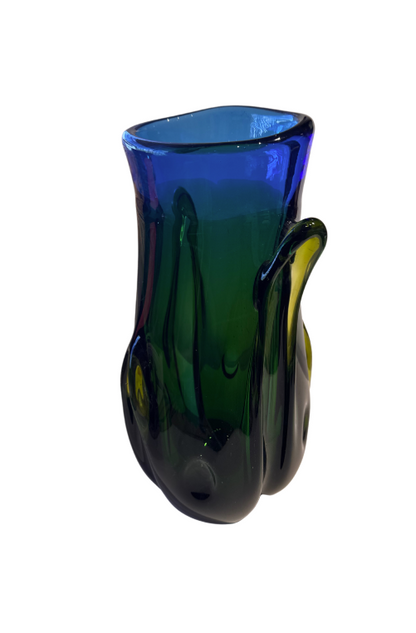Tall, sculptural glass vase with a deep emerald green body, rounded base, and thick cobalt blue rim. Raised, flowing glass accents extend along the sides, incorporating translucent yellow-green details. The vase has an irregular oval opening and a glossy, reflective surface.