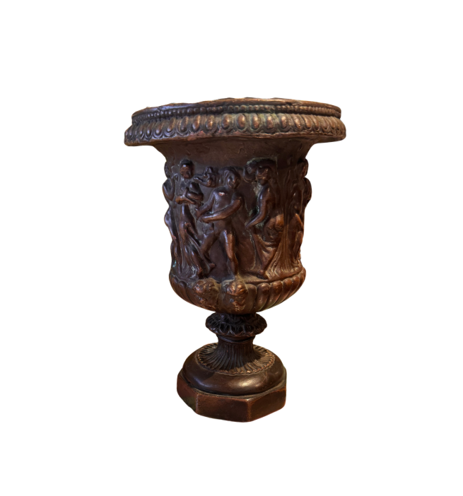 Ornate Neoclassical-style decorative urn with a dark bronze finish, raised classical figures, scrolling foliage, sculptural masks, a wide patterned rim, and a fluted pedestal base. 