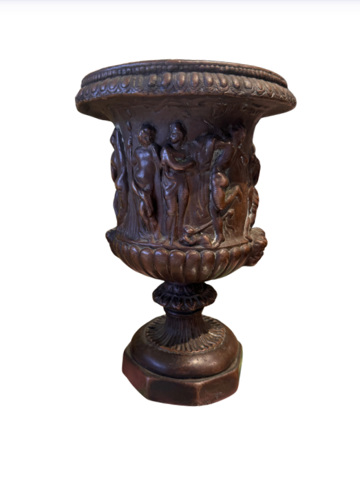 Ornate Neoclassical-style decorative urn with a dark bronze finish, raised classical figures, scrolling foliage, sculptural masks, a wide patterned rim, and a fluted pedestal base. 