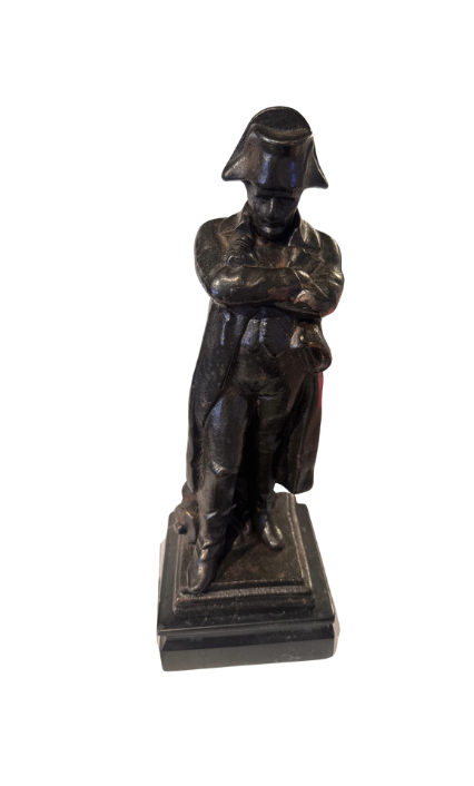 Front View of Dark cast iron statue depicting Napoleon Bonaparte standing with his arms crossed, wearing a bicorne military hat, long overcoat, and boots. The figure stands on a stepped rectangular black marble base.