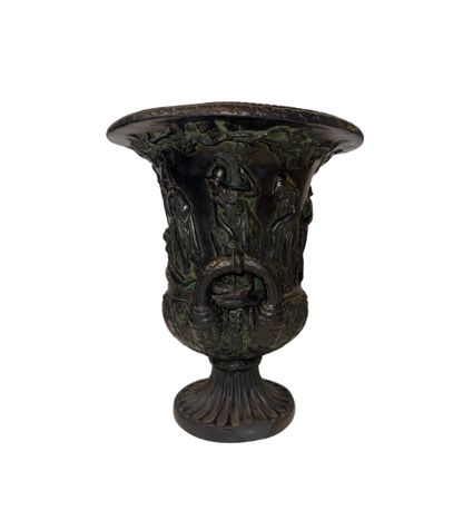 Side View, Black faux-bronze Neoclassical Medici urn with green patina accents, measuring 11 inches tall and 9 inches in diameter. The Campana-shaped vessel features a wide flared rim with egg-and-dart detailing, raised Greco-Roman figures in various poses, grapevine and leaf borders, and two reeded loop handles with bearded mask decorations. An intricate floral and acanthus leaf design surrounds the lower bowl, which rests on a fluted circular pedestal base.