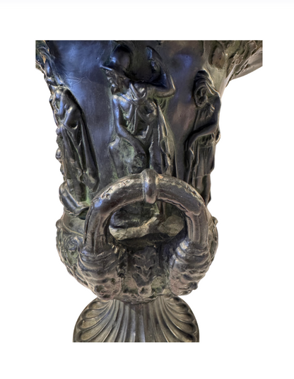 Close up View, Black faux-bronze Neoclassical Medici urn with green patina accents, measuring 11 inches tall and 9 inches in diameter. The Campana-shaped vessel features a wide flared rim with egg-and-dart detailing, raised Greco-Roman figures in various poses, grapevine and leaf borders, and two reeded loop handles with bearded mask decorations. An intricate floral and acanthus leaf design surrounds the lower bowl, which rests on a fluted circular pedestal base.