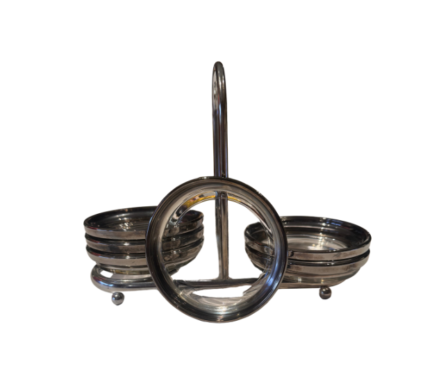Side view of a vintage silver-tone coaster holder showing its curved central handle, stacked glass coasters, and small ball feet.