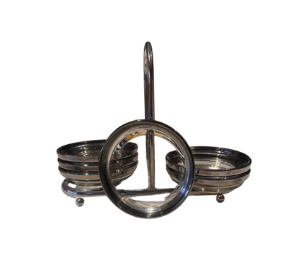 Side view of a vintage silver-tone coaster holder showing its curved central handle, stacked glass coasters, and small ball feet.