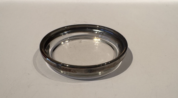 Close-up side view of an individual vintage glass coaster showing its shallow round profile and silver fade rim.
