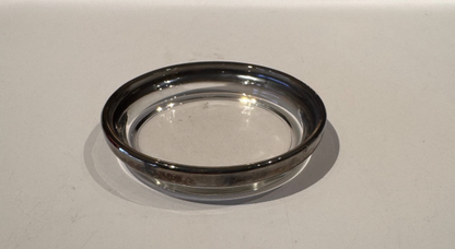 Close-up side view of an individual vintage glass coaster showing its shallow round profile and silver fade rim.