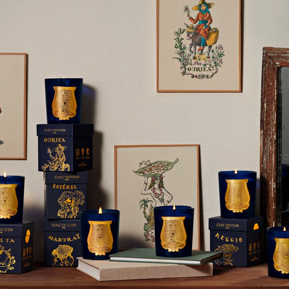 Trudon blue glass candles and navy gift boxes styled on a shelf with framed illustrations
