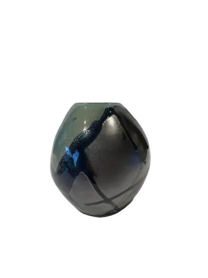 A small glossy ceramic vase with a rounded, rounded-ribbed shape, featuring a dark charcoal gray to black glaze with subtle blue and green iridescent shifts near the base, set against a plain white background.